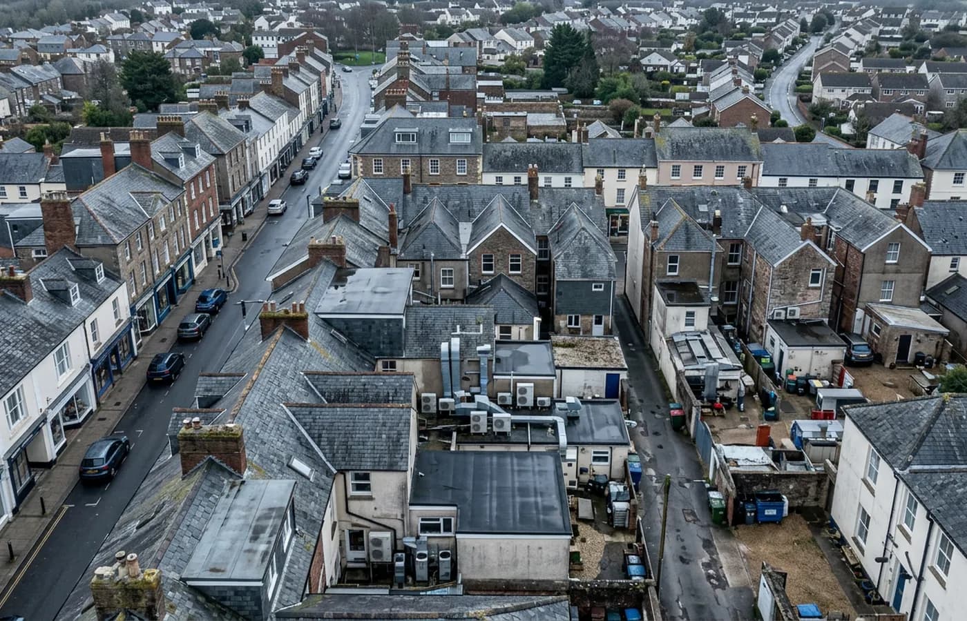 A Devon market town commercial street from the air, shops below and offices above, slate pitches, parapets and flat roofed rear extensions
